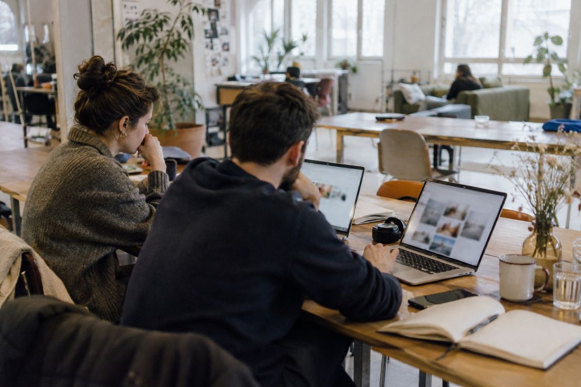 Eine Frau und ein Mann arbeiten in einem hellen Gemeinschaftsbüro nebeneinander an zwei Laptops.